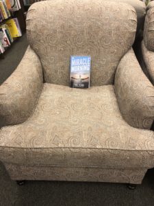 an oversized brown patterned chair holds a blue book entitled "The Miracle Morning" 